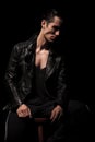 Rocker in black leather jacket posing seated in dark studio Royalty Free Stock Photo