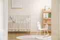 Rocking horse on rug in white kid`s bedroom interior with rabbit poster above cradle