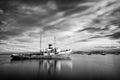 Rocks and a completely calm sea in the foreground with a ship aground with mountains in the background Royalty Free Stock Photo