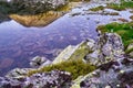 Rocks with green lichens, purple sunset light, and a mountain peak reflecting in Lake Bucura, Retezat Mountains Carpathians