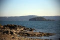 Rocks outcropping in Lake Bolsena with the green Martana island and the coast in the background, Capodimonte, Viterbo, Tuscia, Laz