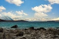 Rocks in turquoise water, waves in Lake Tekapo, background is Mount Cook Mountains. On a beautiful cloudy day on the South Island Royalty Free Stock Photo