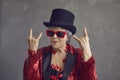 Funny crazy senior grey-haired lady in top hat showing rock-n-roll hand sign