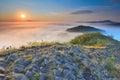 Rocky basalt peak on hill. Forest valley full of gentle fog and Sun above heavy mist. Royalty Free Stock Photo