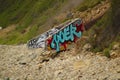 A rocky beach with a lush green hillside and graffiti painted on the walls of the storm drain