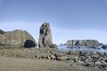 A rocky beach with a tall, dark basalt formation in the center, surrounded by smaller rocks under a clear blue sky Royalty Free Stock Photo