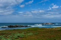 Rocky blue Pacific ocean coastal landscape with waves breaking against the rocks under a dramatic partly cloudy sky Royalty Free Stock Photo