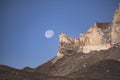 Rocky cliffs in the mountains rise with peaks against the background of the moon and the blue morning sky Royalty Free Stock Photo