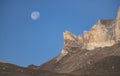 Rocky cliffs in the mountains rise with peaks against the background of the moon and the blue morning sky Royalty Free Stock Photo