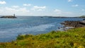 Rocky coastal meadow with green grass, the lighthouse on Gun Rock and the Atlantic Ocean in the background