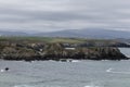 a rocky coastline with a cloudy sky, a light blue ocean with small waves, and distant hills Royalty Free Stock Photo