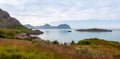 Picturesque grass covered rocky bay of the Norwegian fjord overlooking the distant mountains that are reflected in the surface of Royalty Free Stock Photo
