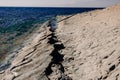 A rocky gentle slope of a mountain shore with a large long crack extending into the blue water of the sea