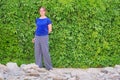 Rocky ground, ivy-covered wall and a brunette girl with glasses. Young woman on green leaf wall background, copyspace. A beautiful Royalty Free Stock Photo
