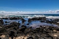 Rocky Hawaiian beach. Rocks, tidepool, sand. Wave and blue ocean in distance. Blue sky and clouds. Royalty Free Stock Photo