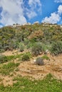 Rocky hill with a dirt road in front under a blue sky with white clouds and a modern villa on top Royalty Free Stock Photo