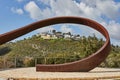 Rocky hill with a dirt road in front under a blue sky with white clouds and a modern villa on top