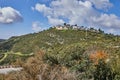 Rocky hill with a dirt road in front under a blue sky with white clouds and a modern villa on top