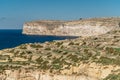 Rocky limestone coastline of Gozo island and Mediterranean Sea with turquoise blue water and caves.Green terraced fields,hills.
