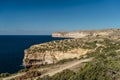 Rocky limestone coastline of Gozo island and Mediterranean Sea with turquoise blue water and caves.Green terraced fields,hills.