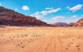 Rocky massifs on red sand desert, bright cloudy sky in background, small 4wd vehicle and camel at distance - typical scenery in Royalty Free Stock Photo