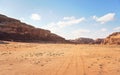 Rocky massifs on red sand desert, bright cloudy sky in background, small 4wd vehicle at distance - typical scenery in Wadi Rum, Royalty Free Stock Photo