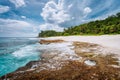 Rocky old reef coastline on tropical Police Bay beach with rolling waves and white clouds on Mahe Island, Seychelles Royalty Free Stock Photo