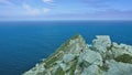 A rocky promontory juts out into the ocean. A small house is visible on the stones.