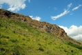 A rocky ridge of a high cliff running along the slope of a gentle hill under a summer cloudy sky Royalty Free Stock Photo