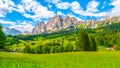 Rocky ridge of Pomagagnon Mountain above Cortina d`Ampezzo with green meadows and blue sky with white summer clouds