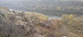 Rocky river bank among hills overgrown with vegetation, granite stones among dry yellowed grass Royalty Free Stock Photo