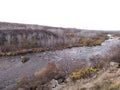 Rocky river bank among hills overgrown with vegetation, granite stones among dry yellowed grass Royalty Free Stock Photo