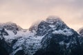 Rocky rugged snowy mountain peaks covered in glowing clouds and haze in sunset in winter in New Zealand, Milford Sound