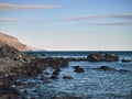 Rocky seashore, calm sea surface, the horizon is clearly visible, light cirrus clouds in the sky Royalty Free Stock Photo