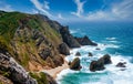 Rocky shore of the Atlantic Ocean. View of high cliffs, foamy waves and sandy beach. Sunny summer seascape. Portuguese riviera. In Royalty Free Stock Photo