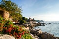 Rocky shore of Sairee beach Koh Tao. Thailand. Large and small boulders are scattered along the shore. Bush with flowers in the