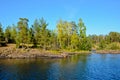 Rocky shore with yellow and green forest. The blue, calm water of the lake. Clear, sunny, blue sky Royalty Free Stock Photo