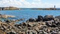 Rocky shoreline with Cromwell`s Barracks, a sailboat and the lighthouse on Gun Rock in the background