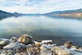 Rocky shoreline in foreground with view of calm lake and snow covered mountains in distance Royalty Free Stock Photo