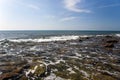 Rocky Shoreline Under Blue Sky With Gentle Waves Breaking on Stones Royalty Free Stock Photo
