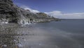 A rocky shoreline, with a white lighthouse on a headland. The beach is Bracelet Bay, Mumbles, south Wales Royalty Free Stock Photo