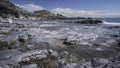 A rocky shoreline, with a white lighthouse on a headland. The beach is Bracelet Bay, Mumbles, south Wales Royalty Free Stock Photo