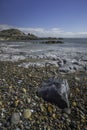 A rocky shoreline, with a white lighthouse on a headland. The beach is Bracelet Bay, Mumbles, south Wales Royalty Free Stock Photo