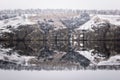 Rocky snow-covered shore in the reflection of the river