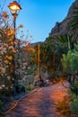 Rocky trail surrounded with fence and flowers under orange lantern on the sunset in Masca village