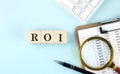 ROI - acronim - RETURN ON INVESTMENT word on wooden cubes on blue background with chart and keyboard