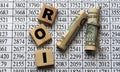 ROI - acronym on cubes on paper background with numbers and banknotes