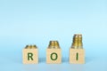 ROI or return on investment letters on wooden blocks in blue background with increasing stack of coins. Increase in profit