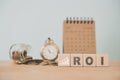 ROI, text and increasing graph on wooden cube block with blurred coins, vintage clock and calendar for