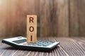 ROI, Return On Investment Word on Wood Block on Top of Calculator